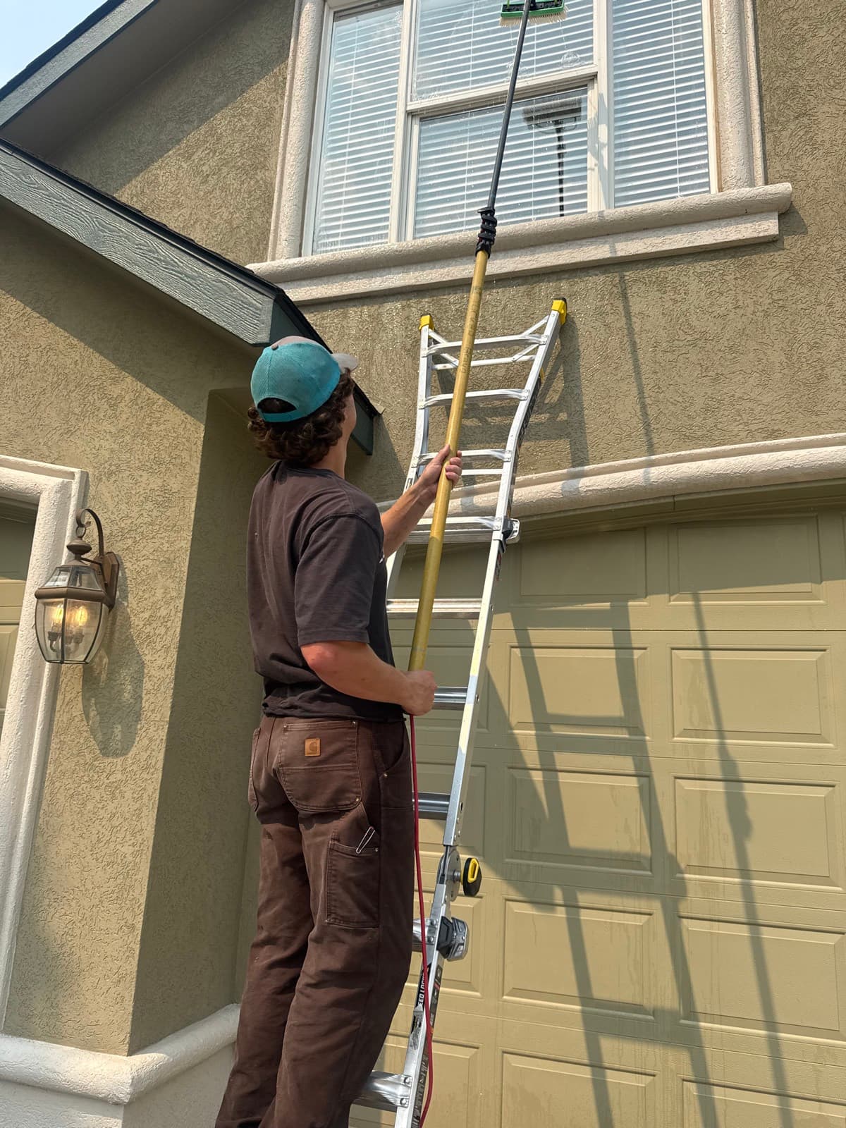 Technician on a ladder cleaning upper-story windows with a water-fed pole